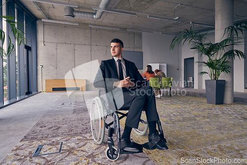 Image of Businessman in a wheelchair commands attention, symbolizing resilience and success amidst a dynamic modern office environment.