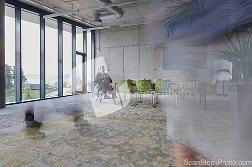 Image of A businessman in a wheelchair sits at a table in a large, modern office, while his colleagues gather around, their steps blurred, symbolizing inclusivity, support, and unity in the face of challenges.