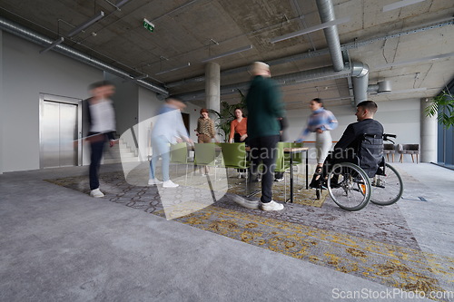 Image of A businessman in a wheelchair sits at a table in a large, modern office, while his colleagues gather around, their steps blurred, symbolizing inclusivity, support, and unity in the face of challenges.