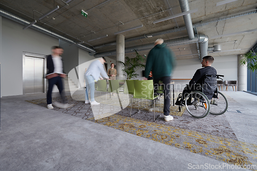 Image of A businessman in a wheelchair sits at a table in a large, modern office, while his colleagues gather around, their steps blurred, symbolizing inclusivity, support, and unity in the face of challenges.