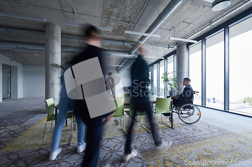 Image of A businessman in a wheelchair sits at a table in a large, modern office, while his colleagues gather around, their steps blurred, symbolizing inclusivity, support, and unity in the face of challenges.