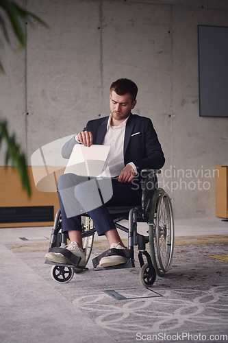 Image of A businessman with disability in a wheelchair using laptop in a modern office