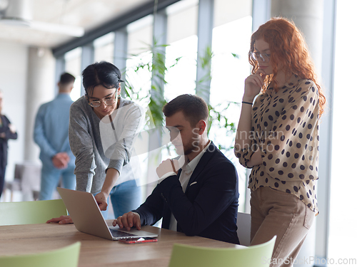 Image of A businessman engaging in a discussion about sales statistics with his two female colleagues while they examine the data on a laptop in a modern office setting