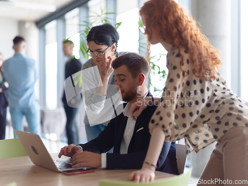 Image of A businessman engaging in a discussion about sales statistics with his two female colleagues while they examine the data on a laptop in a modern office setting