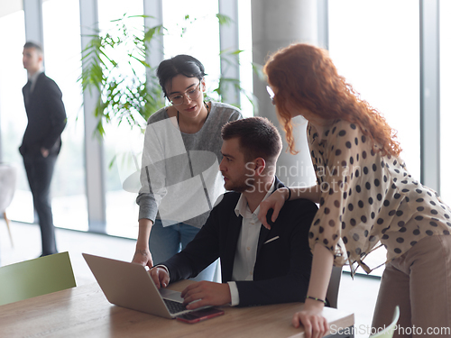 Image of A businessman engaging in a discussion about sales statistics with his two female colleagues while they examine the data on a laptop in a modern office setting