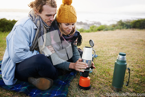 Image of Lets get this coffee warmed up. a young couple warming up a pot of coffee outdoors.