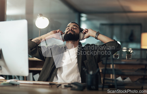 Image of Calming sounds take care of late night stress. a young businessman using headphones during a late night at work.