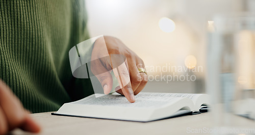 Image of Closeup hand, reading and a bible for faith, spiritual support or hope from scripture. House, table and a person with a book for worship, trust or education on God, Jesus or learning about religion