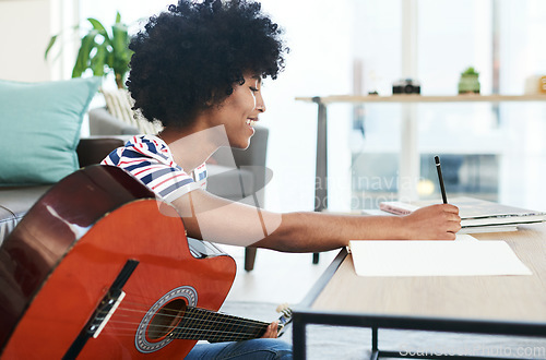 Image of I enjoy making my own music. a woman writing in her notebook while playing the guitar at home.