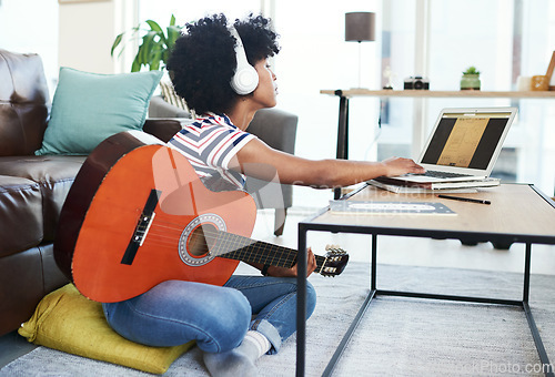 Image of This song needs a bit of tweaking. a woman using her laptop while playing the guitar at home.