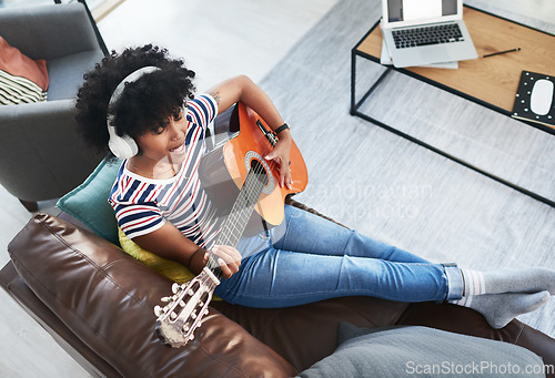 Image of Playing the guitar makes me feel good. a woman wearing headphones while playing the guitar at home.