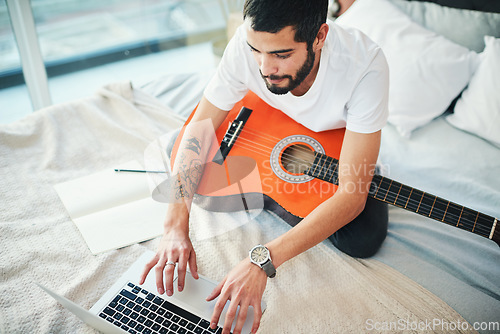 Image of Im taking virtual lessons to learn more about playing the guitar. a man using his laptop while playing the guitar at home.