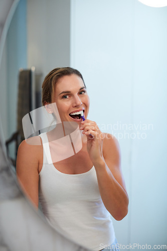 Image of I prioritise my oral health, do you. an attractive young woman brushing her teeth in front of her bathroom mirror.