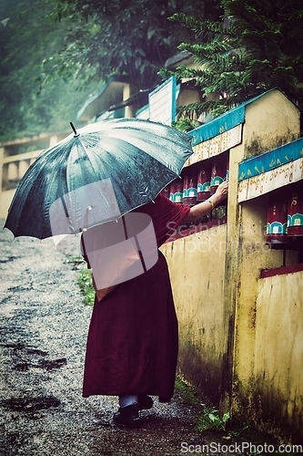 Image of Buddhist monk with umbrella spinning prayer wheels