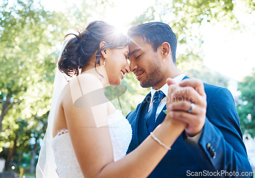 Image of Bride and groom holding hands and touching foreheads while dancing outside. Mixed race newlyweds enjoying romantic moments on their wedding day. Happy young romantic couple sharing their first weddin