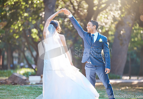 Image of Joyful bride and groom sharing a dance in nature. Groom spins his bride during romantic dance at park on their wedding day