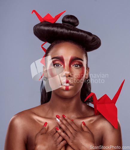 Image of Less division, more integration. Studio shot of a beautiful young woman wearing Asian inspired makeup and posing with origami against a grey background.