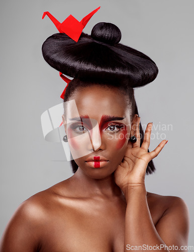 Image of Whatever your look, wear it like you mean it. Studio shot of a beautiful young woman wearing Asian inspired makeup and posing with origami against a grey background.