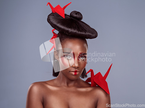 Image of Africa meets Asia. Studio shot of a beautiful young woman wearing Asian inspired makeup and posing with origami against a grey background.