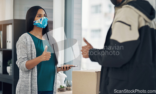 Image of Thats why youre the best. a masked young woman showing thumbs up while receiving a delivery at home.