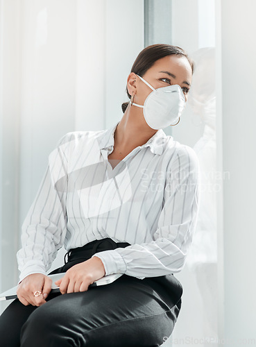 Image of Will business ever be the same again. a masked young businesswoman looking out of a window in a modern office.