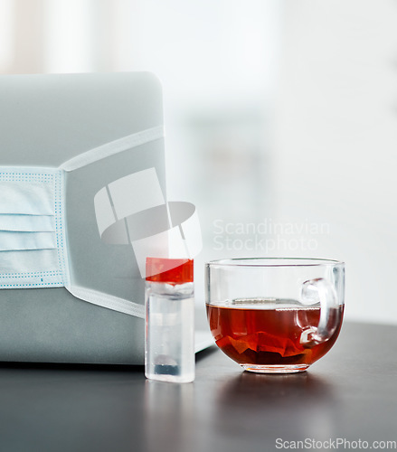 Image of Must haves to make it through the pandemic. a laptop, mask, hand sanitiser and herbal tea on a desk in a modern office.