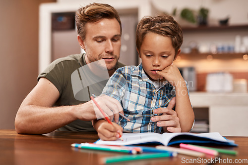 Image of Youre doing well, buddy. a man sitting with his son while he does his homework.