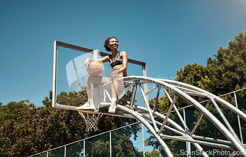 Image of Do you have what it takes to become the best. a sporty young woman sitting on a basketball hoop on a sports court.