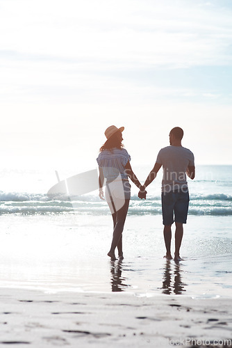 Image of The beach sets the perfect background to their love. Rearview shot of a young couple walking along the beach.