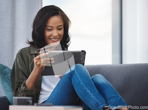 Image of Who can resist a good bargain. an attractive young woman using a digital tablet and credit card on the sofa at home.