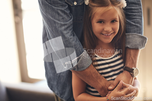 Image of Dads always there to show that her cares. Portrait of an adorable little girl standing with her father’s arms around her at home.