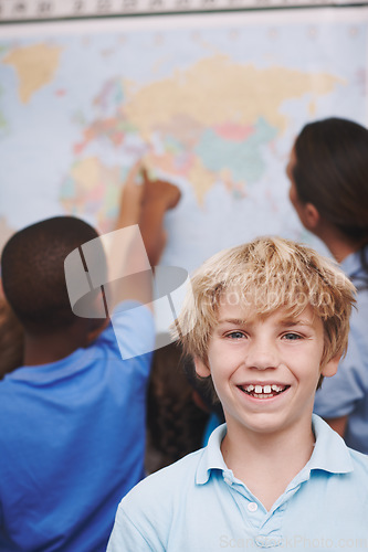 Image of Im going to travel the world one day. A young boy standing in the classroom as his friends and teacher look over a world map.