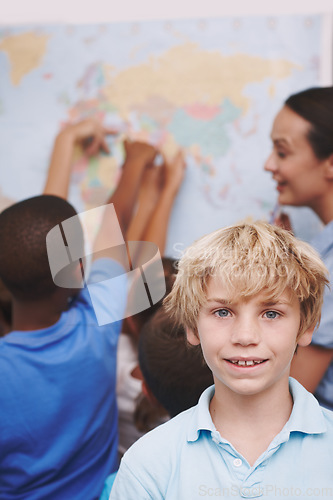 Image of Excited about geography. A young boy standing in the classroom as his friends and teacher look over a world map.