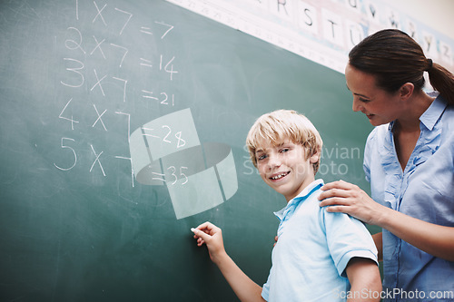 Image of Shes always there to help. A pretty teacher standing at the blackboard with a young student and helping him with his maths.