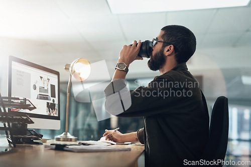 Image of A bit of coffee keeps him in the game. a young businessman having coffee and using a computer during a late night in a modern office.