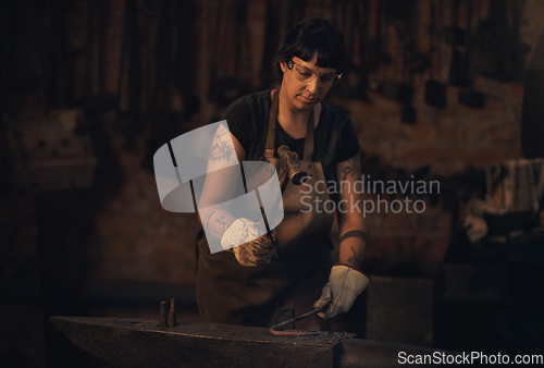 Image of Hard work is always the way. a young woman hitting a hot metal rod with a hammer in a foundry.