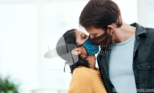 Image of Flirting in 2020 Will you quarantine with me. a young couple kissing each other while wearing masks at home.