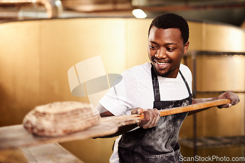 Image of He bakes with passion. a male baker removing freshly baked bread from the oven.