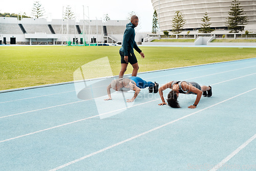 Image of Hold it Hold it. Full length shot of two attractive young athletes doing press-ups on a track field while their coach watches.