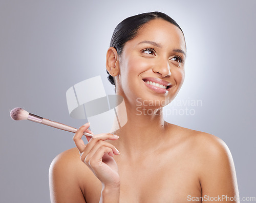 Image of How should I do my makeup today. an attractive young woman standing alone in the studio and feeling playful while holding a makeup brush.