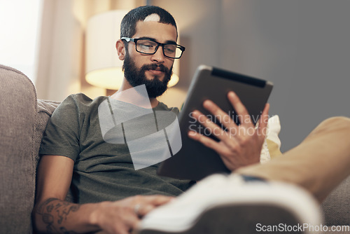 Image of Loaded with all the info he needs. a young man using a digital tablet on the sofa at home.