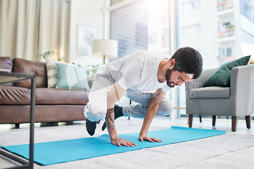 Image of Keep boredom at bay with a yoga session. a handsome young man practising yoga in his living room at home.