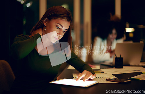 Image of Ive been sitting like this for hours. a businesswoman experiencing neck pain while using a digital tablet in an office at night.