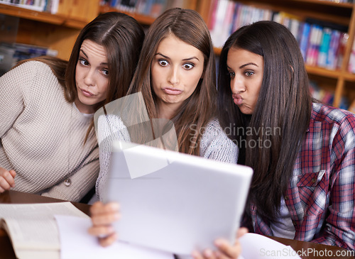 Image of Taking a duck face break. three friends sitting in the library taking photos of themselves with a digital tablet.