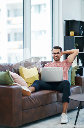 Image of Im staying put but my websites taking off. a young man using a laptop while relaxing on a sofa.