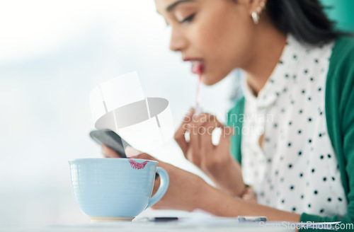 Image of Don’t believe the hype, you can have beauty and brains. a young businesswoman applying lipstick using a smartphone with a smudge of it on a cup at work.