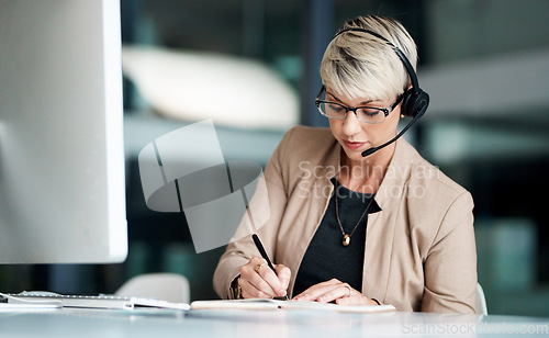Image of Ill be sure to follow-up on that. a young businesswoman wearing a headset while writing notes in an office.