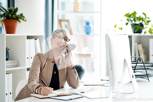 Image of Shes always willing to go the extra mile for her clients. a young businesswoman writing notes while talking on a cellphone in an office.