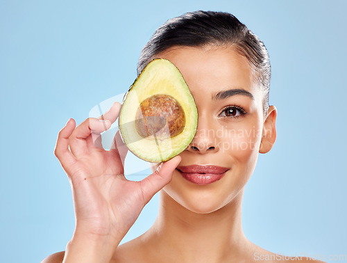 Image of The natural oils in avocados penetrate the skin to nourish and hydrate. Studio portrait of an attractive young woman posing with an avocado against a blue background.