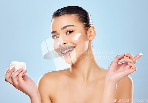 Image of Sunscreen and water are your skins best friend. Studio portrait of an attractive young woman applying moisturiser on her face against a blue background.